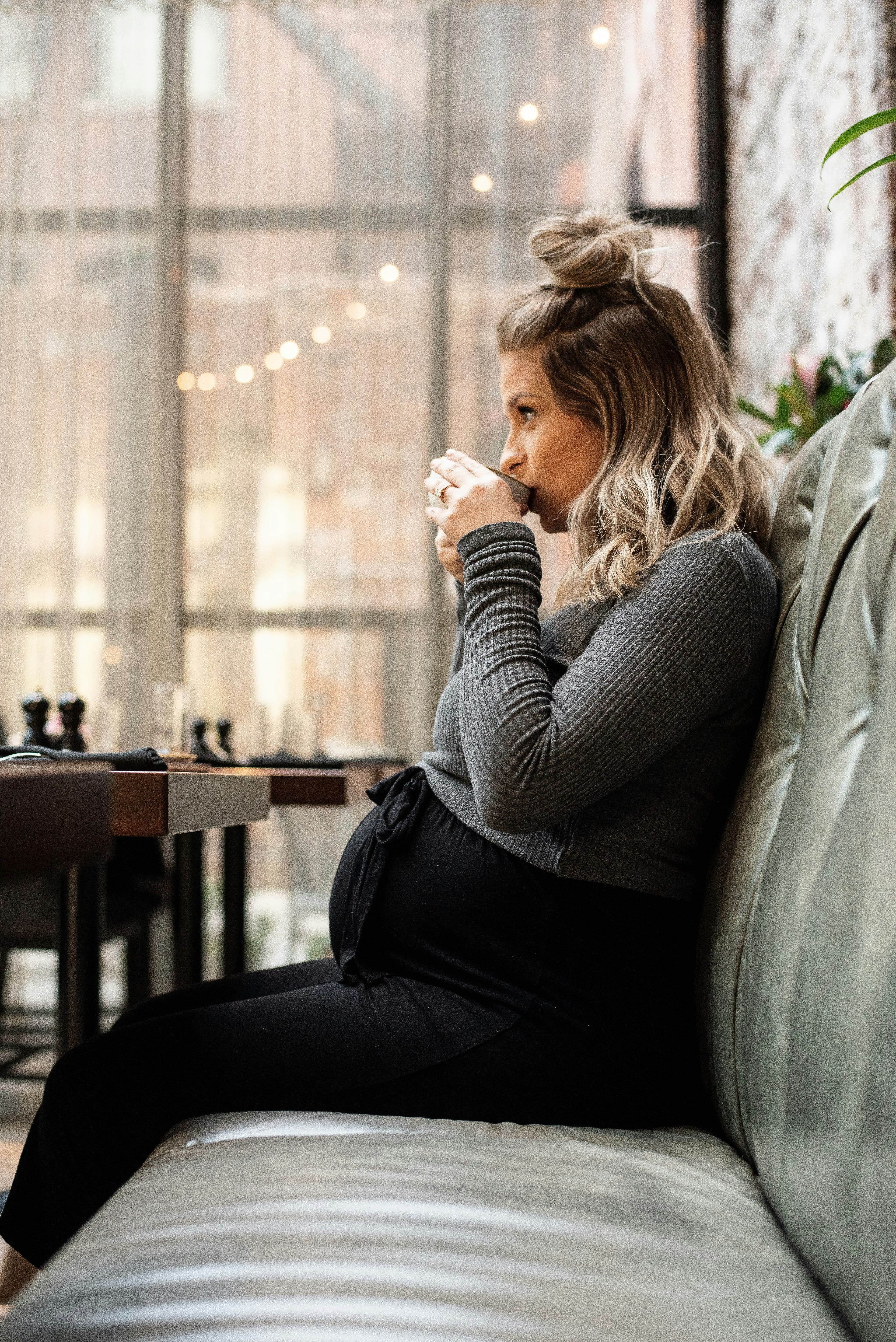A pregnant woman sipping tea by a café window—a small pause for a pregnancy journal note.