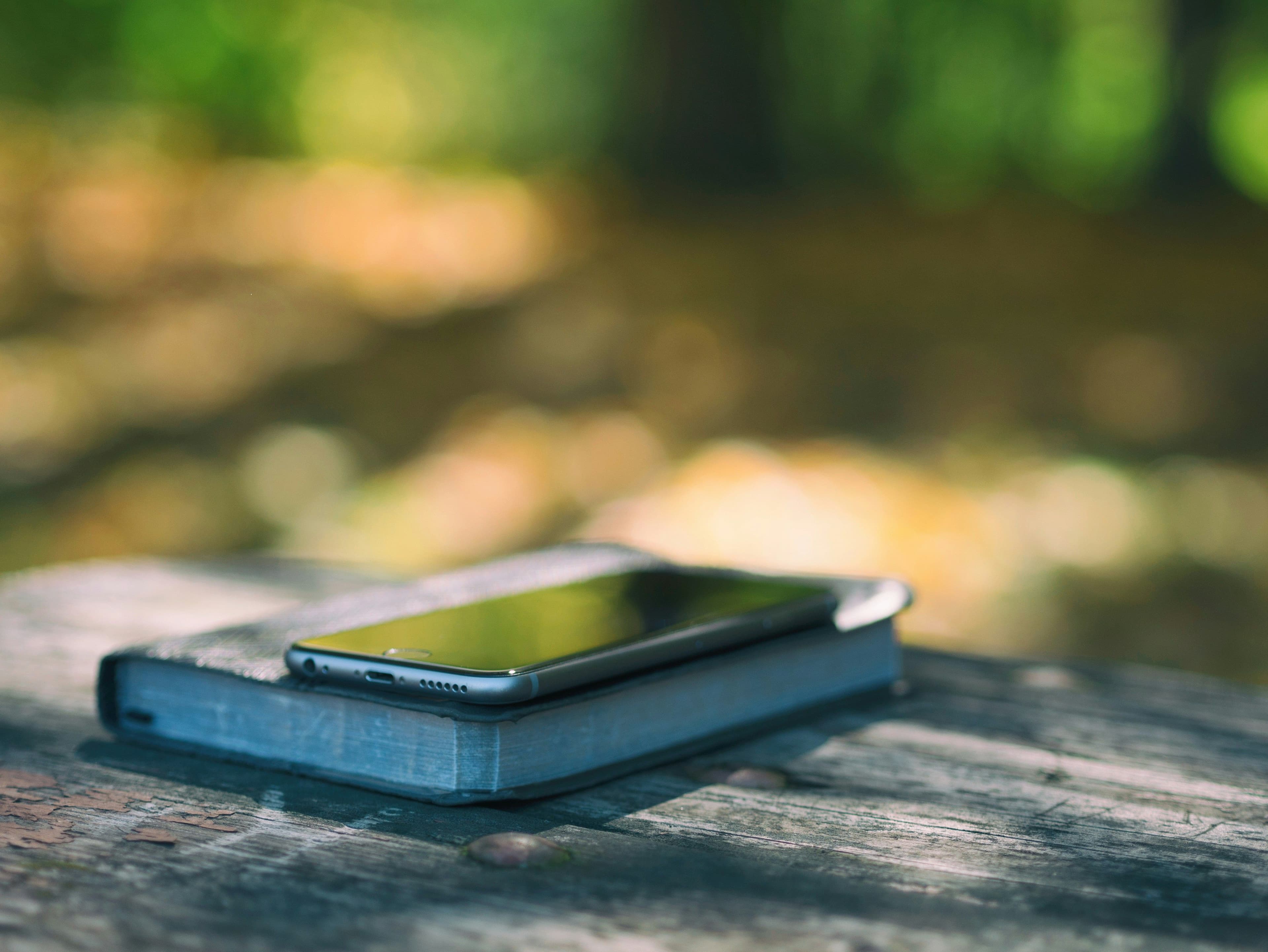 A smartphone resting on a closed journal on a sunlit wooden bench—digital photos waiting to become a first-year book.